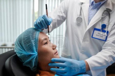 Téléchargez les photos : Image recadrée de chirurgien plastique marquant le visage de la jeune femme avant la chirurgie - en image libre de droit