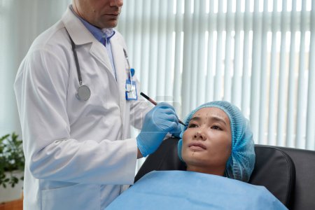 Téléchargez les photos : Femme assise dans la chaise du chirurgien plastique obtenir son visage marqué - en image libre de droit