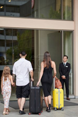 Téléchargez les photos : Famille de trois personnes avec valises marchant jusqu'à l'entrée de l'hôtel - en image libre de droit