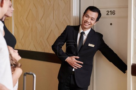 Téléchargez les photos : Enthousiaste gestionnaire d'hôtel ouvrant la porte pour les invités - en image libre de droit