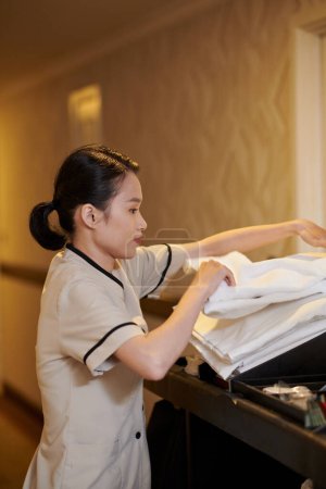 Foto de Joven criada en uniforme cambiando toallas en habitaciones de hotel - Imagen libre de derechos