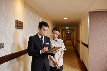Photo for Manager and hotel maid checking list of guests on tablet computer before cleaning rooms - Royalty Free Image