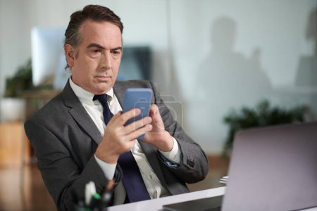 Téléchargez les photos : Homme d'affaires mature sérieux vérifiant les messages texte et les notifications sur smartphone - en image libre de droit