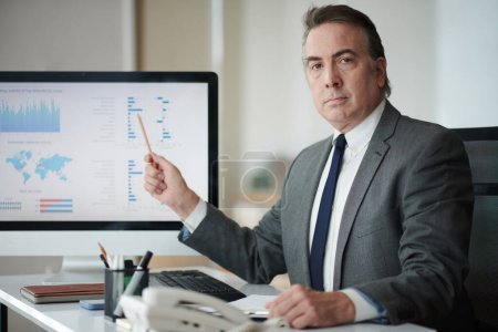 Téléchargez les photos : Portrait d'entrepreneur sérieux pointant vers l'écran d'ordinateur avec le graphique - en image libre de droit