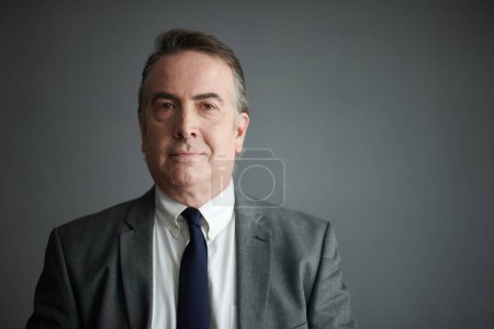 Photo for Portrait of smiling mature businessman standing against grey background - Royalty Free Image