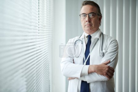 Photo for Portrait of serious confident general practitioner standing at window in medical office - Royalty Free Image