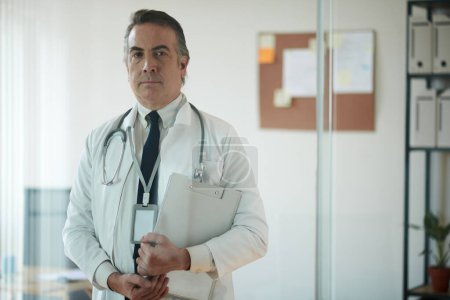 Téléchargez les photos : Portrait d'un médecin généraliste sérieux avec dossier dans un cabinet médical - en image libre de droit