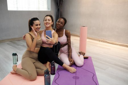 Téléchargez les photos : Joyeuses jeunes femmes en forme prenant selfie après avoir suivi un cours de yoga ensemble - en image libre de droit