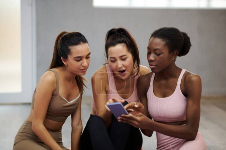 Photo for Young woman showing shocking post on social media to her friends after fitness class - Royalty Free Image
