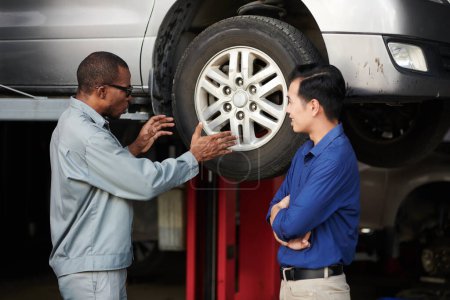 Téléchargez les photos : Mécanicien expliquant au client pourquoi les pneus doivent être équilibrés - en image libre de droit