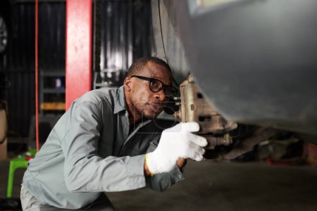 Foto de Mecánico en gafas examinando coche suspendido en garaje - Imagen libre de derechos