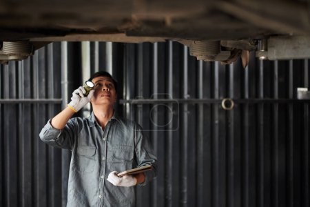 Téléchargez les photos : Travailleur de service de voiture vérifiant le fond suspendu de l'automobile pour les fuites - en image libre de droit