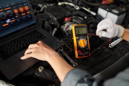 Photo for Closeup image mechanic using multimeter when checking work of car engine - Royalty Free Image