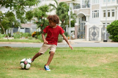 Téléchargez les photos : Enfant actif talentueux jouant au football sur la cour arrière - en image libre de droit