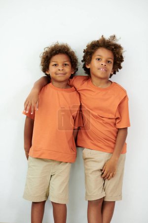 Photo for Portrait of hugging brothers in same clothes leaning on wall and looking at camera - Royalty Free Image