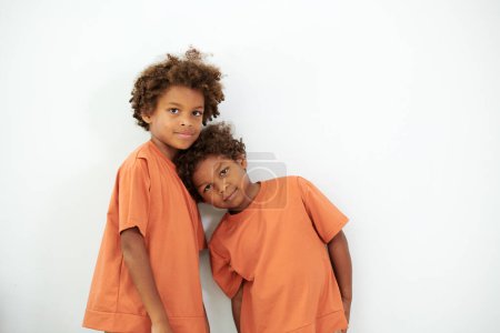 Téléchargez les photos : Deux frères en même t-shirts debout au mur blanc et regardant la caméra - en image libre de droit