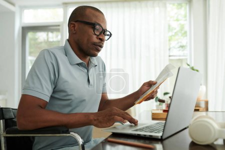 Foto de Hombre negro con discapacidad revisando sus documentos médicos y llenando el formulario en el portátil - Imagen libre de derechos