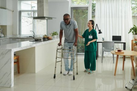 Photo for Social worker controlling patient walking around house with walkers for the first time - Royalty Free Image