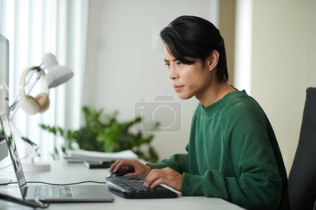 Téléchargez les photos : Pensive jeune développeur de logiciels regardant l'écran d'ordinateur portable, vérifier le code de programmation pour les erreurs - en image libre de droit