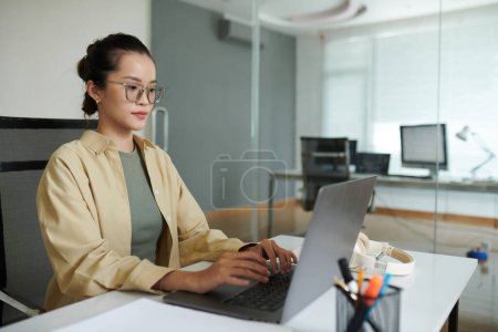 Photo for Young female software developer working on laptop at office desk - Royalty Free Image