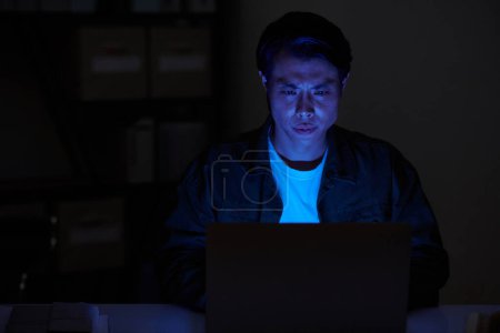 Foto de Retrato del desarrollador de software serio que trabaja en el ordenador portátil en la habitación oscura por la noche - Imagen libre de derechos