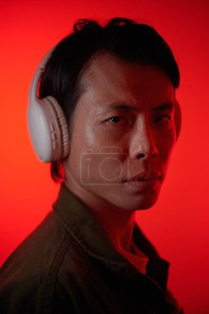 Photo for Portrait of Asian man in headphones standing against bright red background - Royalty Free Image