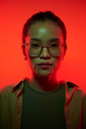 Téléchargez les photos : Portrait de jeune femme asiatique dans des lunettes debout dans la lumière rouge - en image libre de droit