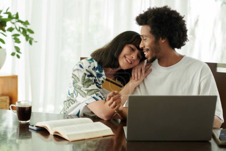 Téléchargez les photos : Joyeux jeune femme gardant la tête sur l'épaule de son mari avec une carte de crédit tout en étant assis devant un ordinateur portable et en commandant des biens en ligne - en image libre de droit