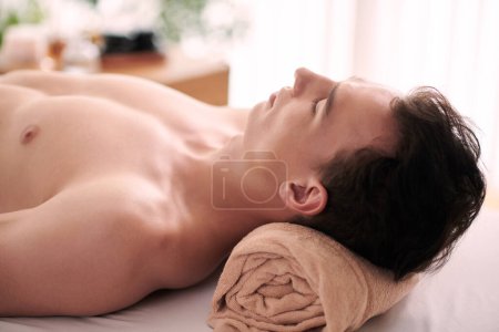 Foto de Hombre joven relajándose en el salón de belleza después de recibir masaje rejuvenecedor en la cara y el cuello - Imagen libre de derechos