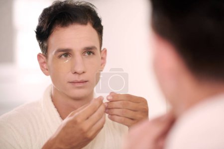 Téléchargez les photos : Portrait de jeune homme appliquant des patchs sous les yeux après la douche du matin - en image libre de droit