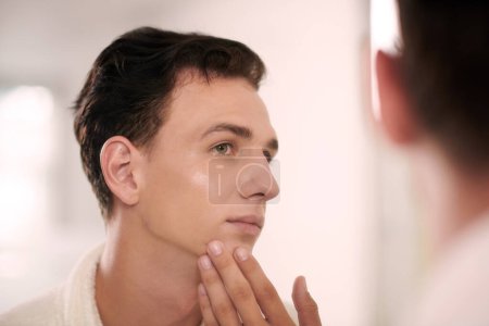 Foto de Retrato de un hombre joven aplicando loción facial abrillantadora después de la ducha nocturna - Imagen libre de derechos