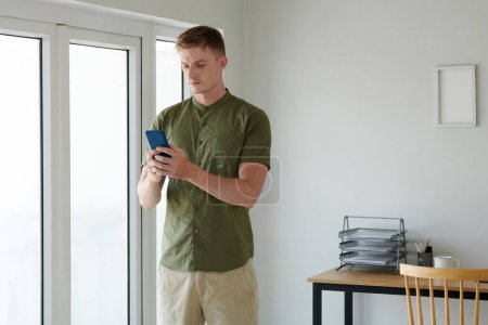 Photo for Frowning young man checking text messages from coworkers in smartphone - Royalty Free Image