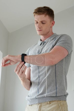 Téléchargez les photos : Jeune homme d'affaires mettant sur montre-bracelet quand gettign prêt le matin - en image libre de droit