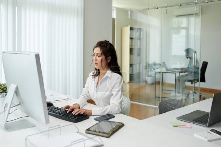 Téléchargez les photos : Jeune femme d'affaires élégante en chemise blanche travaillant sur ordinateur au bureau - en image libre de droit
