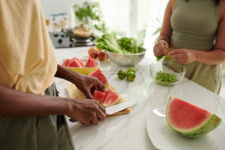 Photo for Woman slicing watermelon when friend making salad - Royalty Free Image