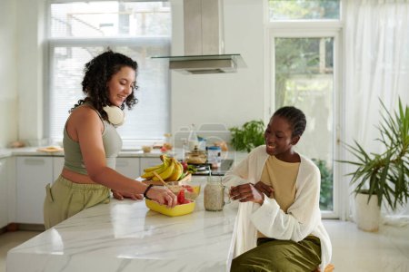 Photo for Smiling girls eating fresh fruits in kitchen for lunch - Royalty Free Image