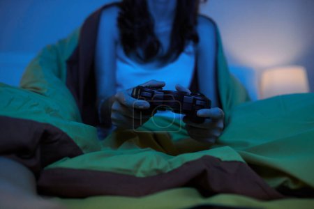 Foto de Imagen recortada de una joven sentada en la cama y jugando videojuegos por la noche - Imagen libre de derechos