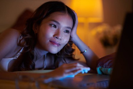 Téléchargez les photos : Portrait de jeune femme souriante regardant de courtes vidéos drôles sur ordinateur portable avant d'aller dormir - en image libre de droit