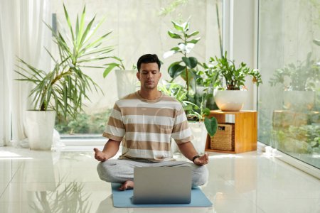 Photo for Calm young man having meditating practice when sitting in front of opened laptop - Royalty Free Image