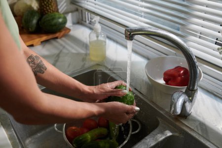 Foto de Manos de mujer enjuagando verduras en fregadero de cocina - Imagen libre de derechos