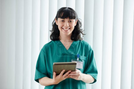 Téléchargez les photos : Portrait d'une infirmière de l'hôpital souriante en blouse tenant un ordinateur tablette - en image libre de droit