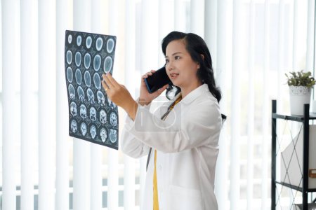 Téléchargez les photos : Un médecin appelle un radiologue pour discuter des radiographies des disques de la colonne vertébrale - en image libre de droit