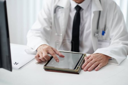 Photo for Doctor zooming image on tablet computer when sitting at desk - Royalty Free Image