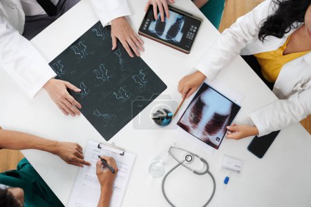 Téléchargez les photos : Groupe de médecins discutant des images radiographiques et remplissant la carte médicale du patient, vue d'en haut - en image libre de droit