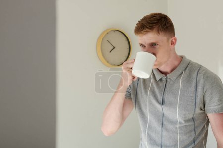 Foto de Hombre bebiendo café de la mañana en la habitación con reloj colgando en la pared - Imagen libre de derechos