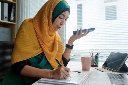 Téléchargez les photos : Concepteur d'interface utilisateur musulman écoutant le message vocal de son collègue et corrigeant le wireframe de l'interface - en image libre de droit