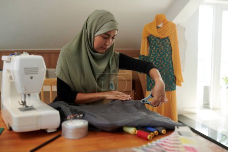 Foto de Costurera musulmana que corta la tela al hacer el vestido para el cliente - Imagen libre de derechos