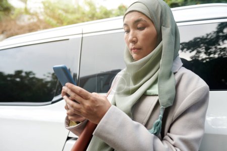 Téléchargez les photos : Femme d'affaires musulmane sérieuse lisant des messages texte de collègues sur smartphone - en image libre de droit