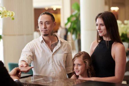 Téléchargez les photos : Famille avec enfant donnant des passeports à la réceptionniste de l'hôtel - en image libre de droit
