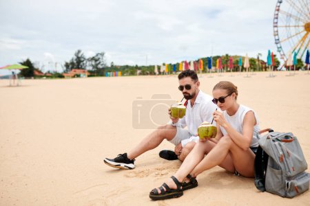 Téléchargez les photos : Couple reposant sur une plage de sable et buvant des cocktails à la noix de coco après une longue promenade - en image libre de droit